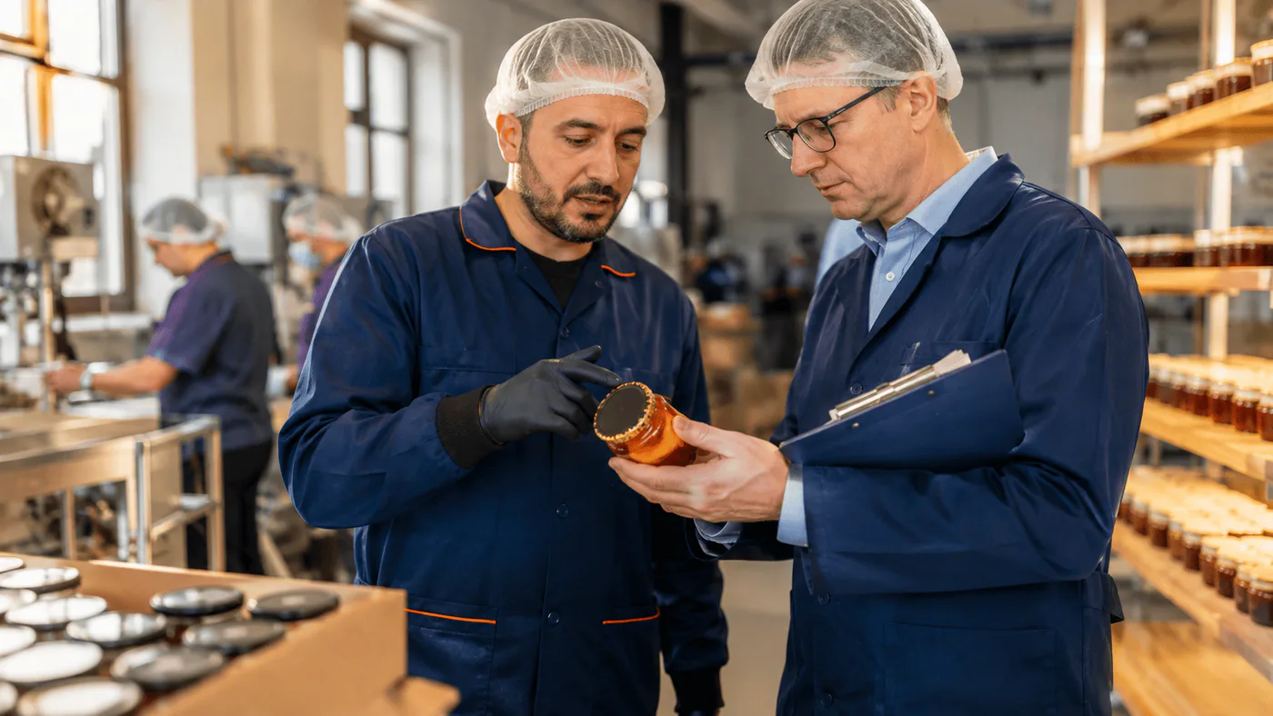 Buyer and factory manager inspect a packaged product on an Armenian production floor while workers operate in the background